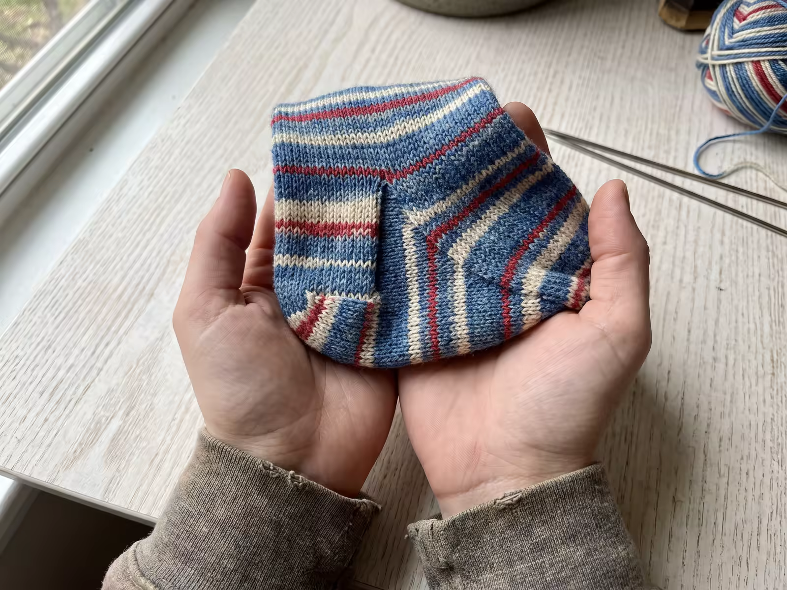 Eine fertige Socke mit ausgeprägter Käppchenferse in der Hand, die Bumerangform ist gut sichtbar.