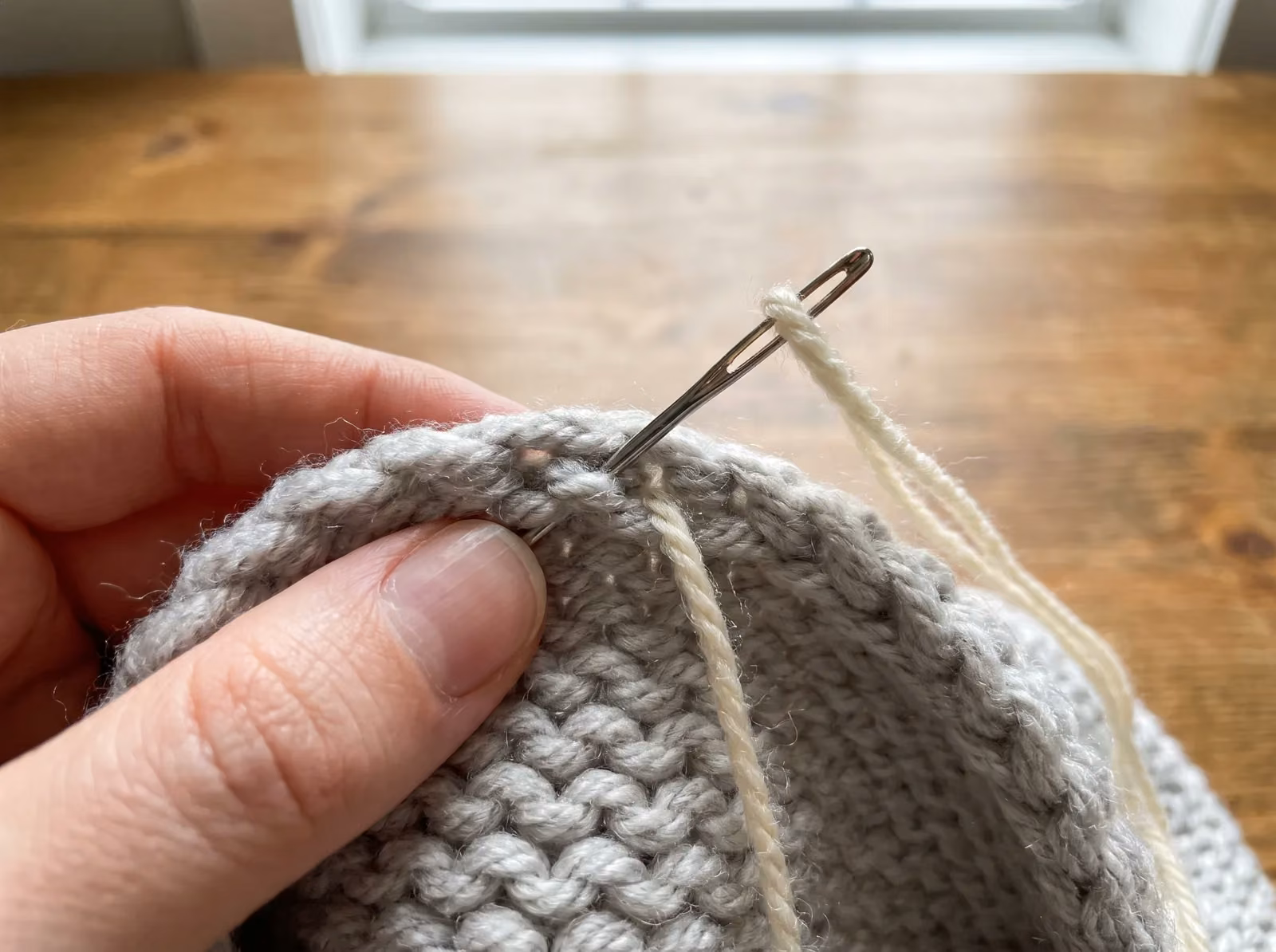 Eine Hand vernäht den letzten Faden mit einer Wollnadel auf der Rückseite