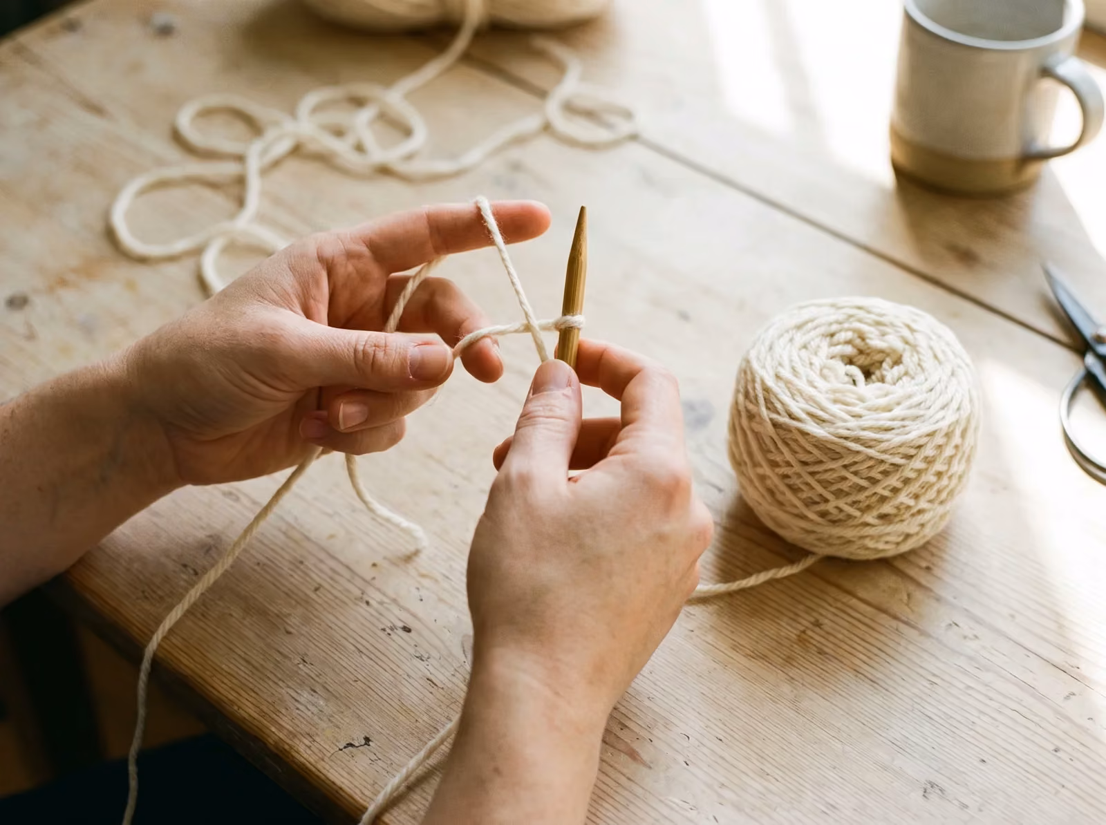 Hände beim Kreuzanschlag auf einer Stricknadel neben einem Wollknäuel
