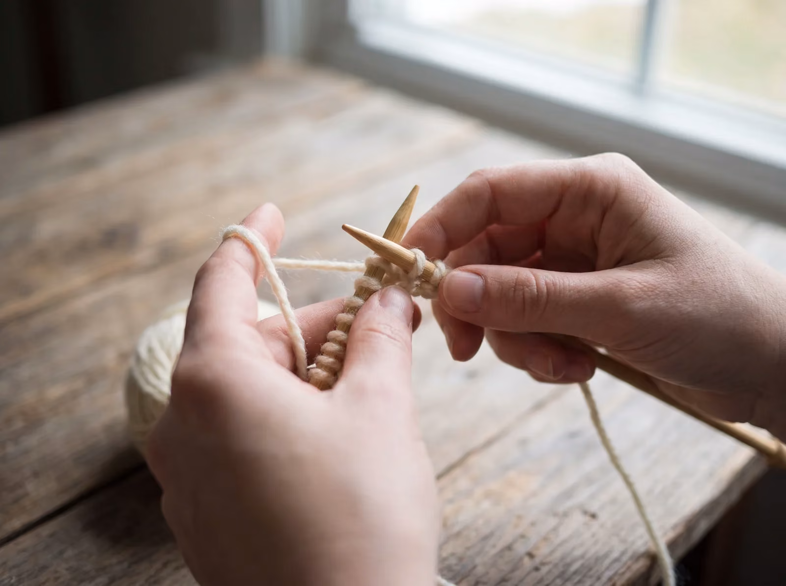 Anfängerhände stricken eine rechte Masche auf geraden Nadeln