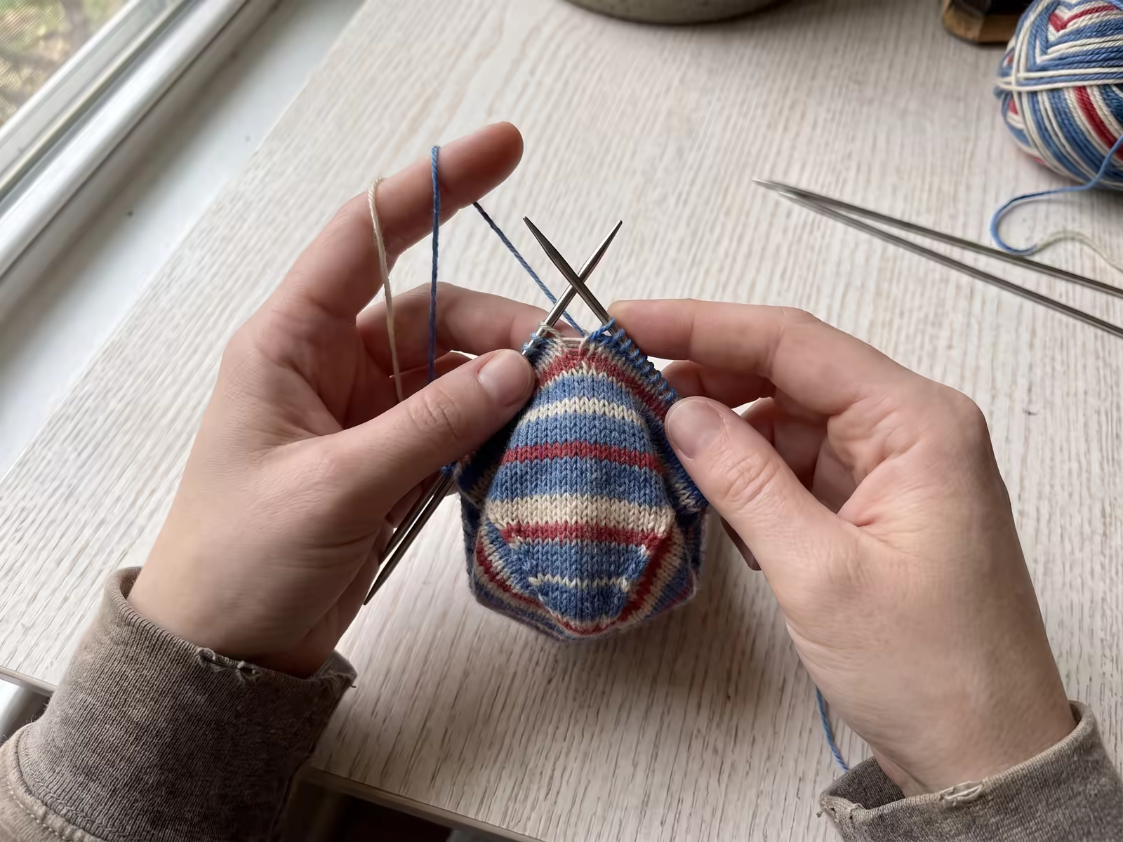 Eine Toe-up-Socke wird von der Spitze aus auf einem Nadelspiel gestrickt, die Maschen sind sichtbar.